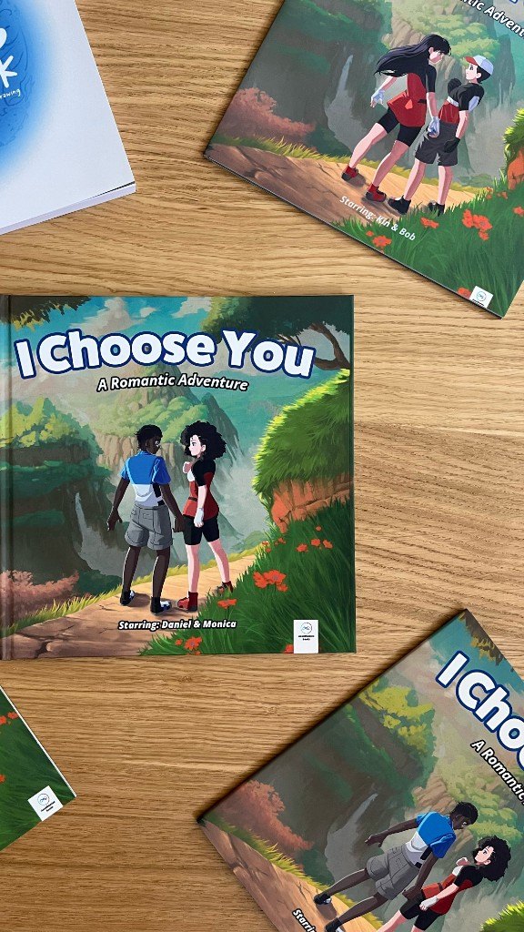Printed copies of I Choose You, starring Daniel & Monica, spread out on a wooden table